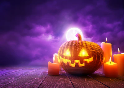 Glowing jack-o'-lantern surrounded by lit candles against a purple moonlit sky on wooden surface