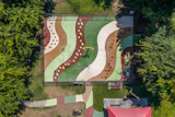 Aerial view of a colorful playground with curved pathways, sand areas, and green spaces surrounded by trees
