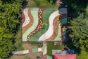 Aerial view of a colorful playground with curved pathways, sand areas, and green spaces surrounded by trees