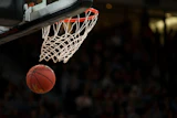 Basketball soaring toward the hoop during a game with white net and blurred crowd in background