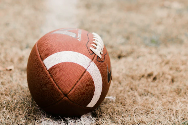 Brown football with white stripes resting on grass and dirt ground