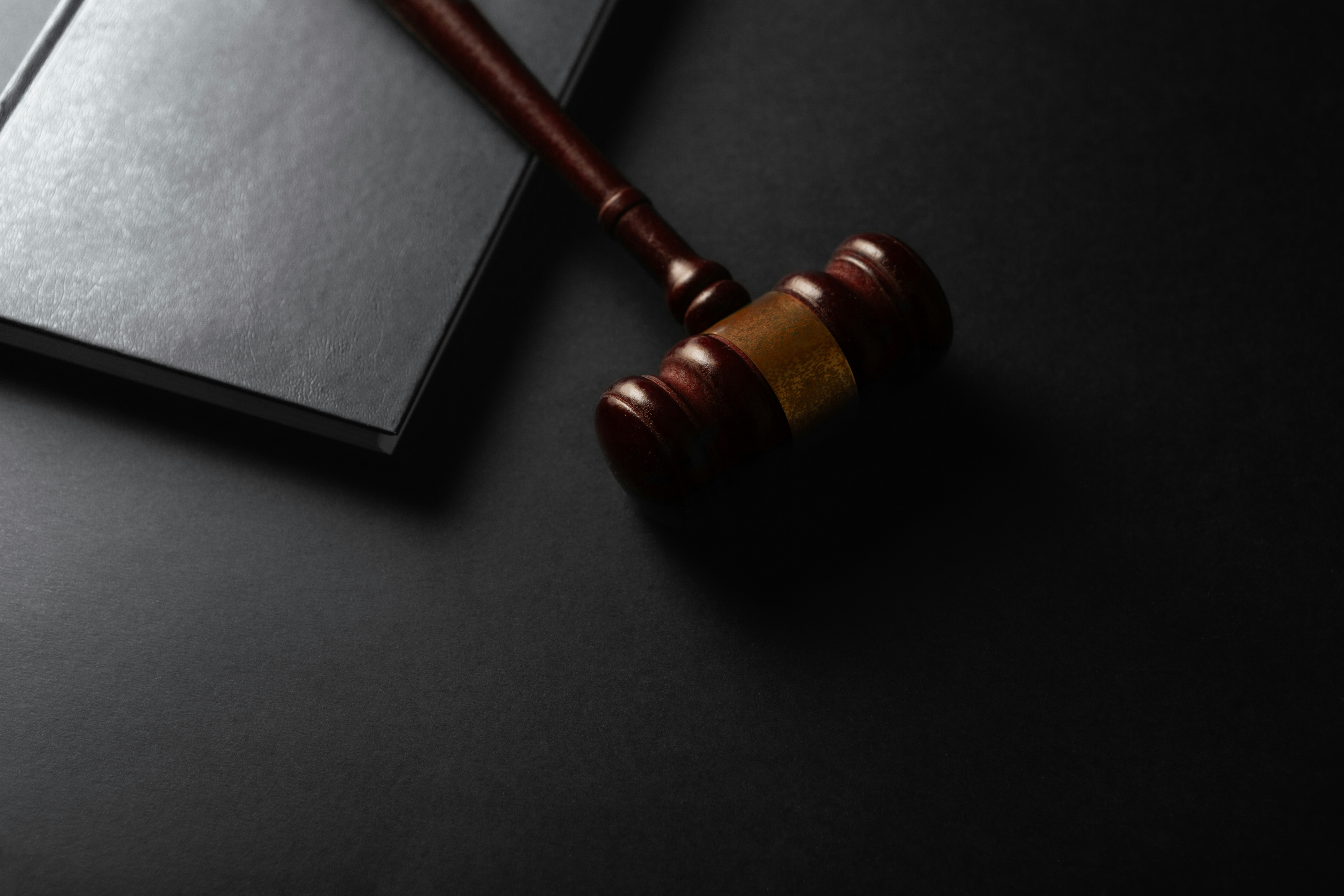 Wooden gavel with brass band next to open notebook on dark surface