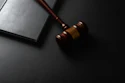 Wooden gavel with brass band next to open notebook on dark surface