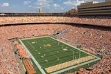 Packed football stadium with orange-clad fans, green field, and yellow end zone during game day
