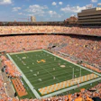 Packed football stadium with orange-clad fans, green field, and yellow end zone during game day