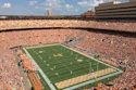 Packed football stadium with orange-clad fans, green field, and yellow end zone during game day