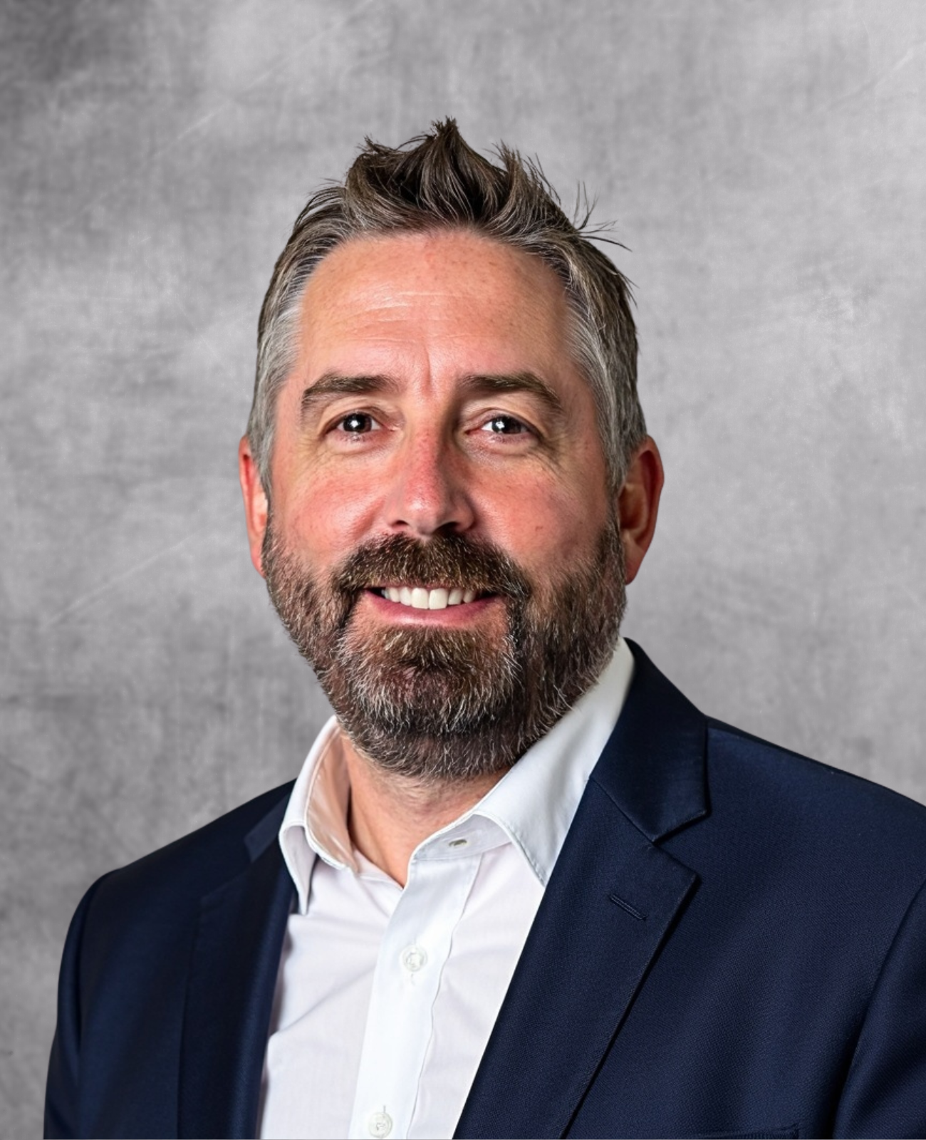 Professional headshot of a bearded man in dark blazer and white shirt smiling at camera