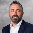 Professional headshot of a bearded man in dark blazer and white shirt smiling at camera
