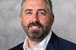 Professional headshot of a bearded man in dark blazer and white shirt smiling at camera