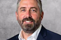 Professional headshot of a bearded man in dark blazer and white shirt smiling at camera